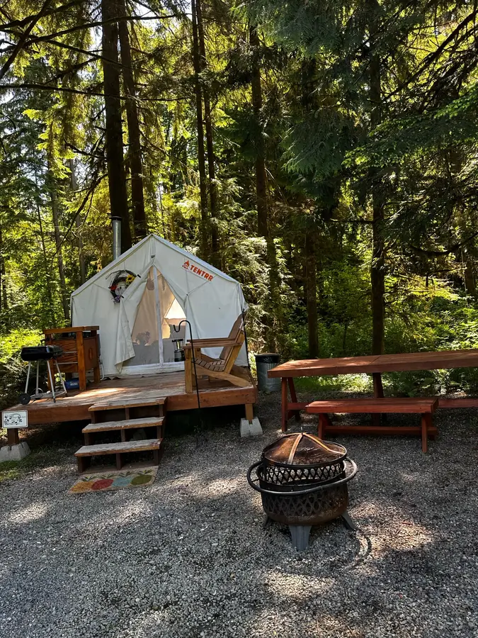 A Fern Gully tent on its wooden deck under the cedars, with a picnic table and fire pit