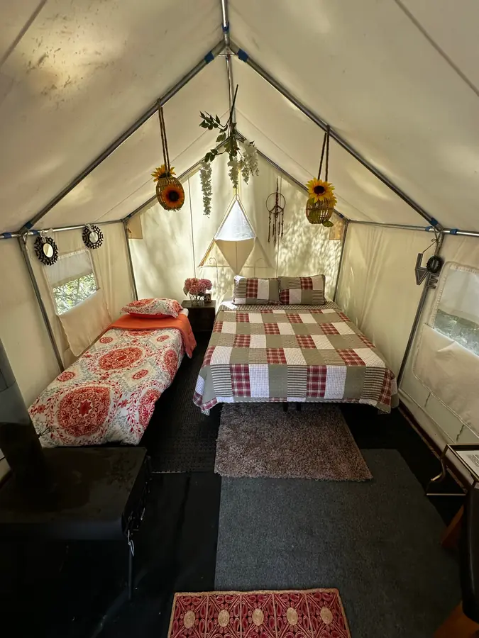 Inside a Fern Gully tent: a queen bed and a cot, with the wood stove and sunflowers overhead