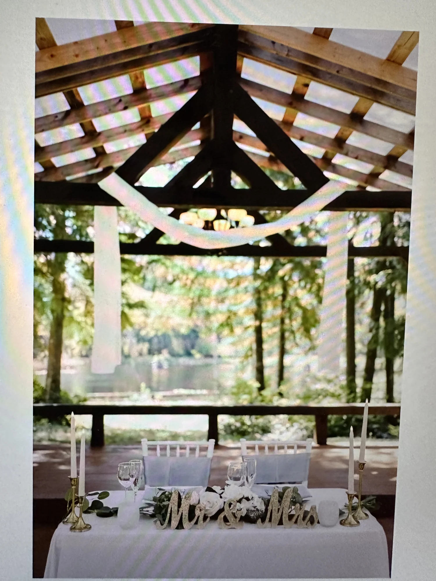 The draped head table under the covered patio, framing the lake beyond
