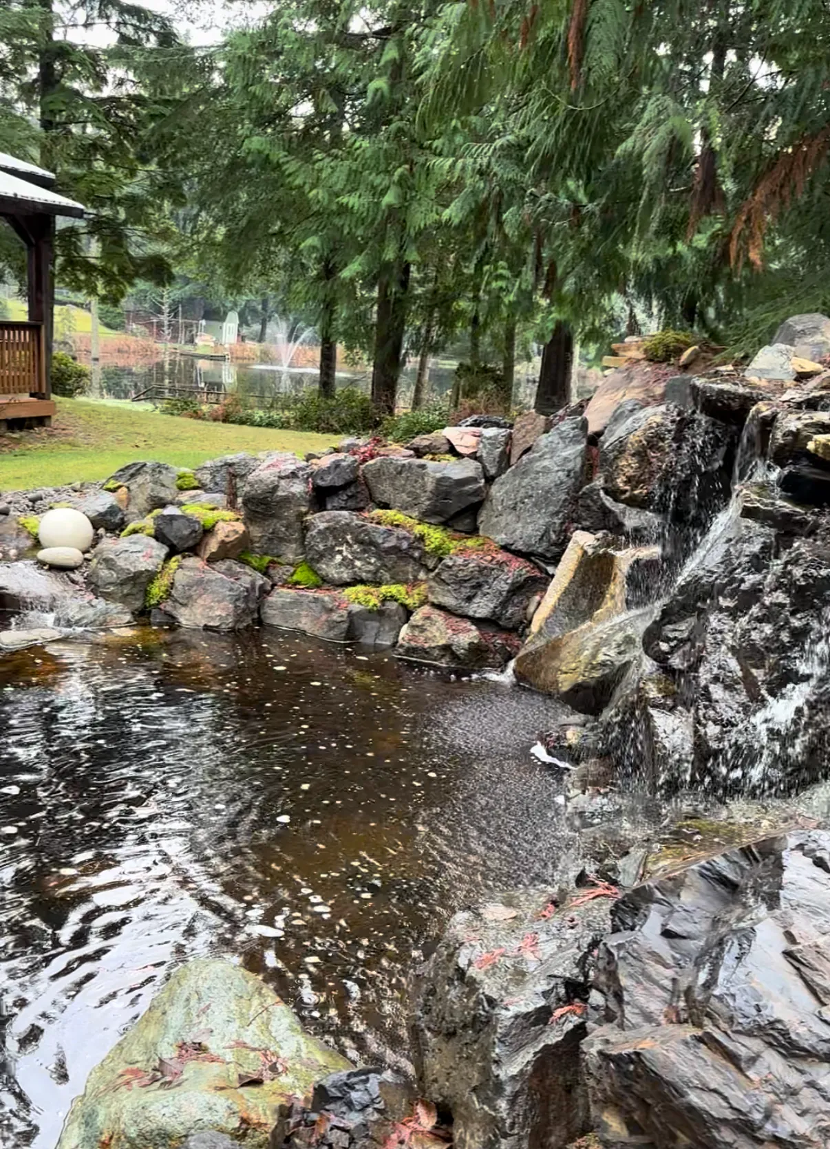 The waterfall tumbling over dark stone beside the covered patio, with the lake and fountain beyond